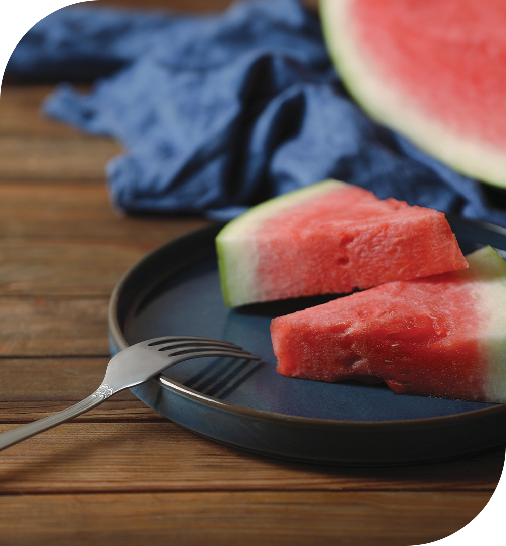[라이프케어] 잘린 수박 두개가 접시 위에 놓여있고 접시 끝에는 포크가 뒤집혀 올려져있습니다. 뒤쪽에는 반 잘린 나머지 수박의 있습니다.